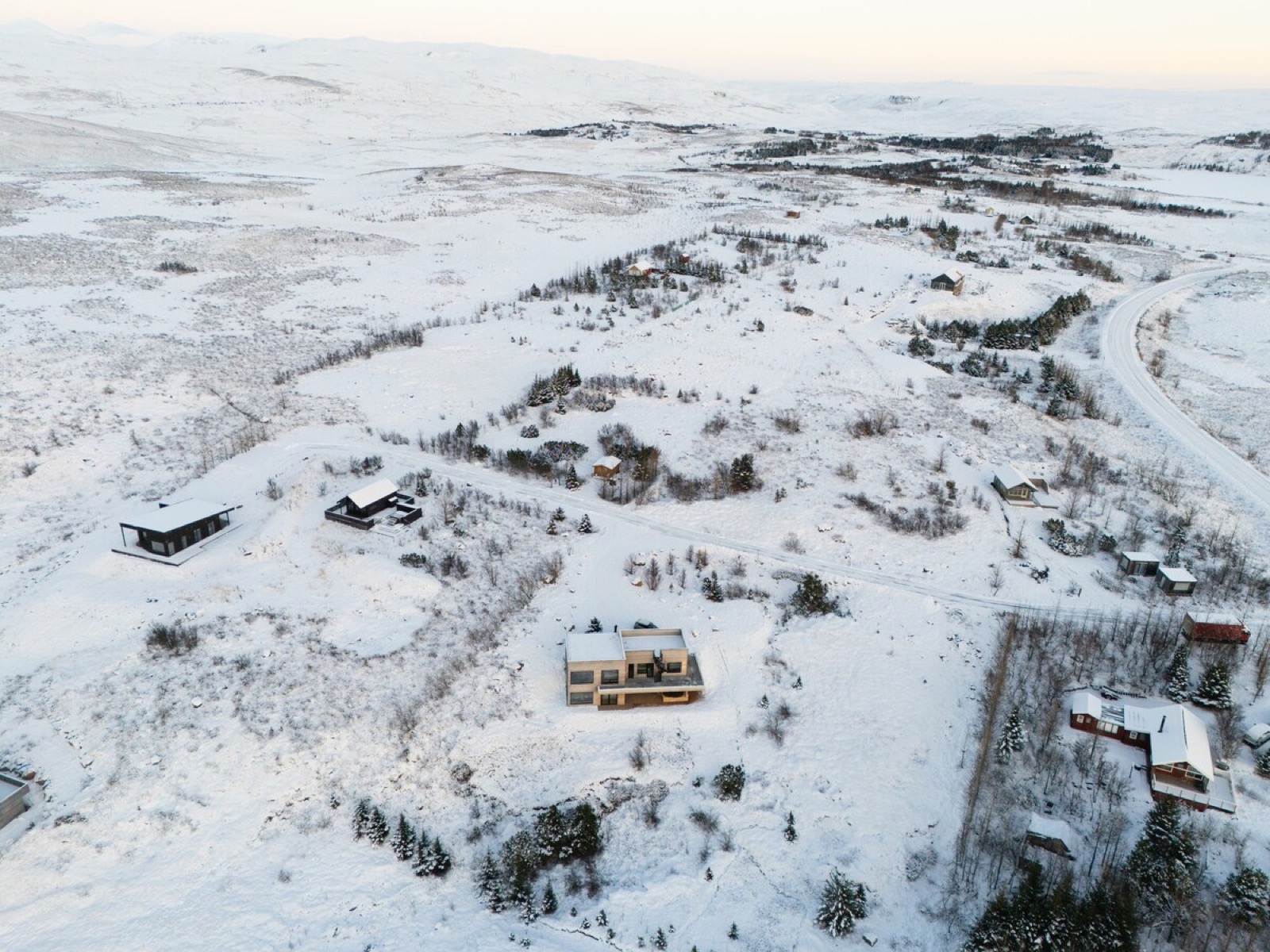 The house and its neighbours on the snow-covered heath from the air, the road running past below